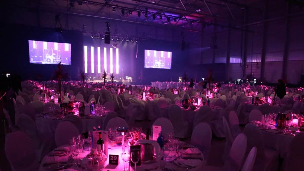 Saal mit Galabestuhlung und Bühne mit LED-Wänden. Alles ist pink beleuchtet.